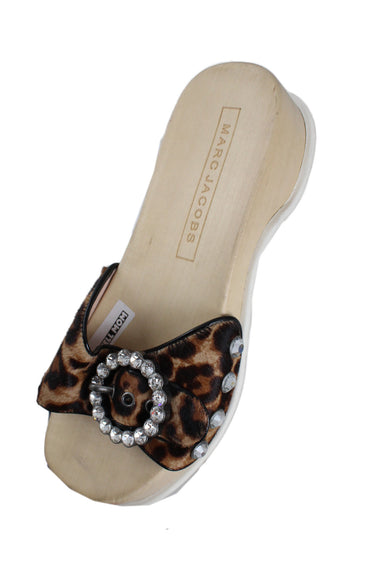 marc jacobs leopard print pony hair blond wood clogs. features large circular rhinestone buckle, rubber sole, single strap across front of foot, rhinestone grommets, and debossed branded wood insole. 