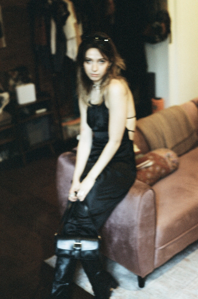 blurry image of model against couch in slip dress holding bag.